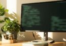 Workspace con monitor LED, terminal Linux borroso y planta albahaca en tonos sage green cremosos