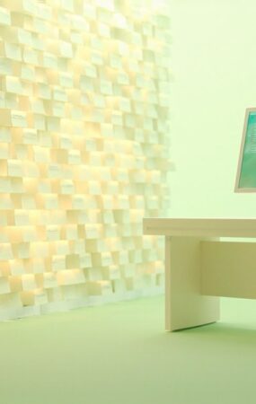 Render 3D editorial de un puesto de trabajo de operaciones de seguridad: un muro de tarjetas de alerta amber que representan la avalancha de reportes de vulnerabilidad entrantes, un monitor slim con un panel de control abstracto y un mueble tipo rack sin marcas sobre una mesa color crema con fondo verde menta claro, luz de estudio brillante, sin texto ni logotipos